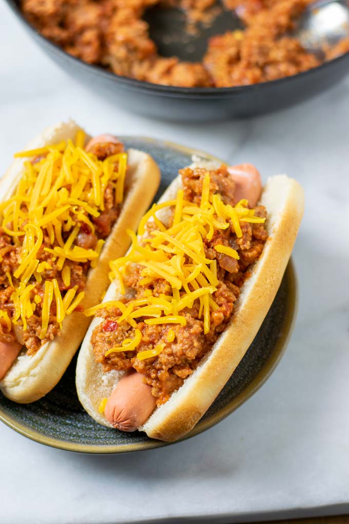 A plate with two hot dogs loaded with the Hot Dog Chili and sprinkled with vegan cheese.