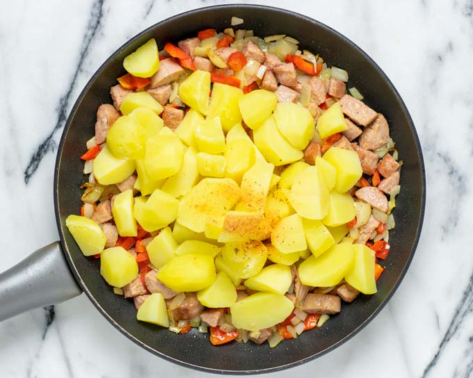 View of the potatoes being added to a pan with the onions and sausage.