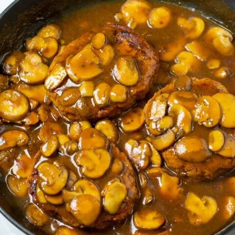 Three Salisbury Steaks in a pan with mushroom gravy.