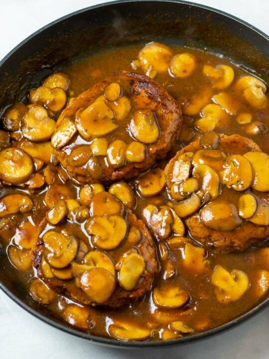 Three Salisbury Steaks in a pan with mushroom gravy.