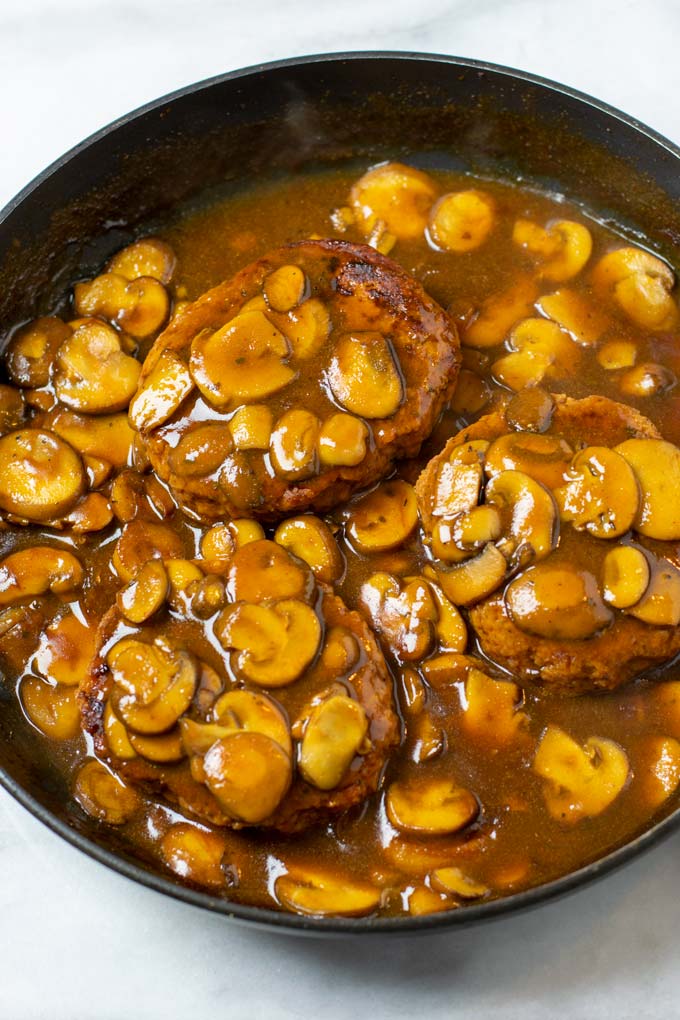 Three Salisbury Steaks in a pan with mushroom gravy.