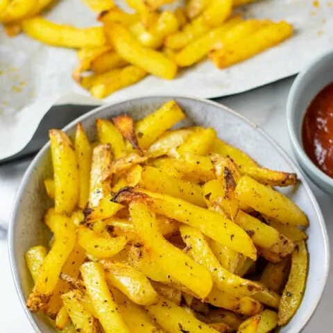 A serving of the Cajun Fries, with a side bowl of ketchup and the baking sheet in the background.