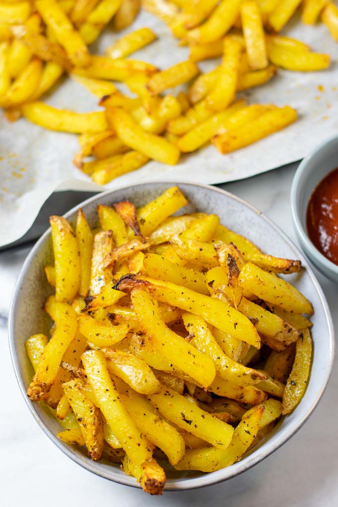 A serving of the Cajun Fries, with a side bowl of ketchup and the baking sheet in the background.