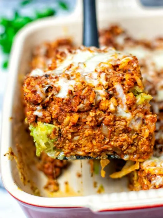 A large spoon is lifting a big portion of the Cabbage Roll Casserole out of the baking dish.