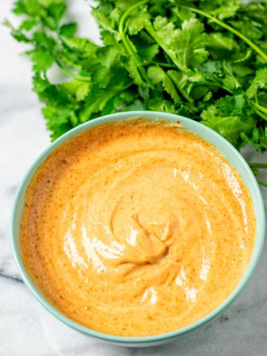 A light green bowl with the creamy Cajun Sauce and some fresh cilantro in the background.