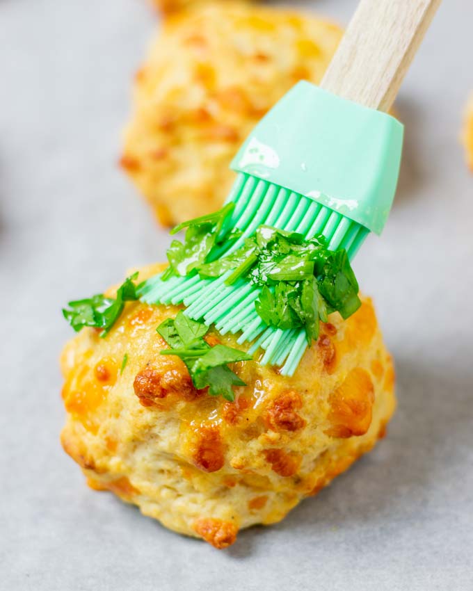 Closeup of a Cheddar Bay Biscuit being coated with garlic butter.