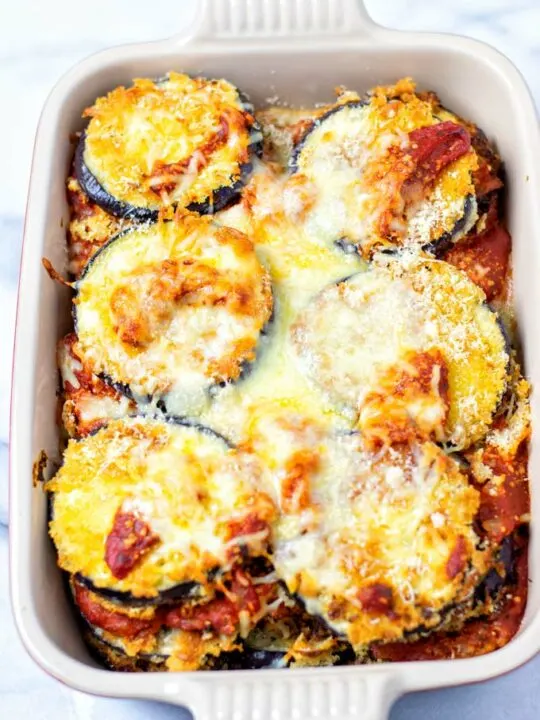 View of the baking dish as the Eggplant Parmesan comes fresh from the oven: layers of eggplant covered with tomato sauce and dairy-free cheese, baked crispy on top.