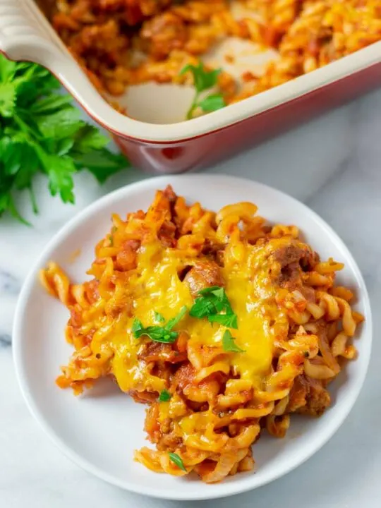 A portion of the Hamburger Casserole with pasta is served on a small white plate. The backing dish is visible in the background.