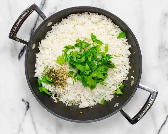 Top view of a large sauce pan filled with leftover white rice, fresh herbs and spices before mixing.