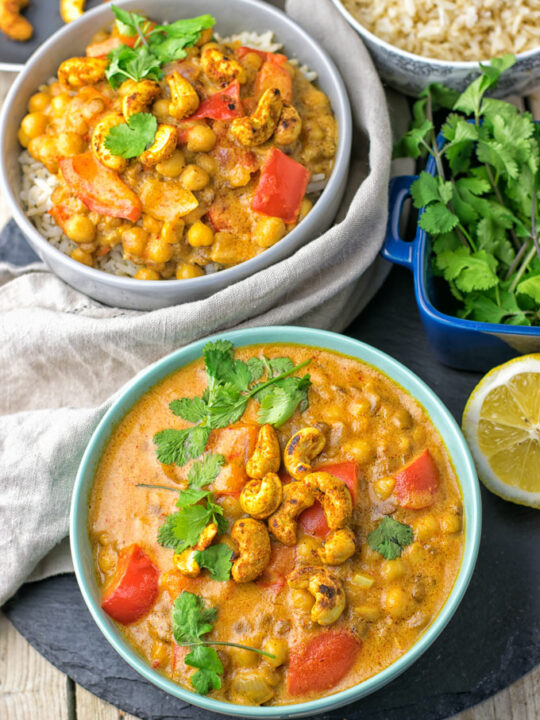 Two bowls of the Lentil Chickpea Yellow Curry, garnished with fresh cilantro and some fresh lemon.