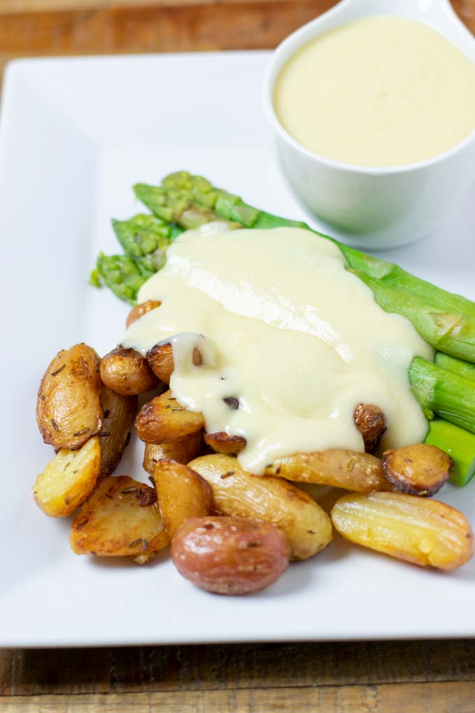 A portion of baked potatoes and green asparagus are served with the Mornay Sauce. A sauce boat is in the background.