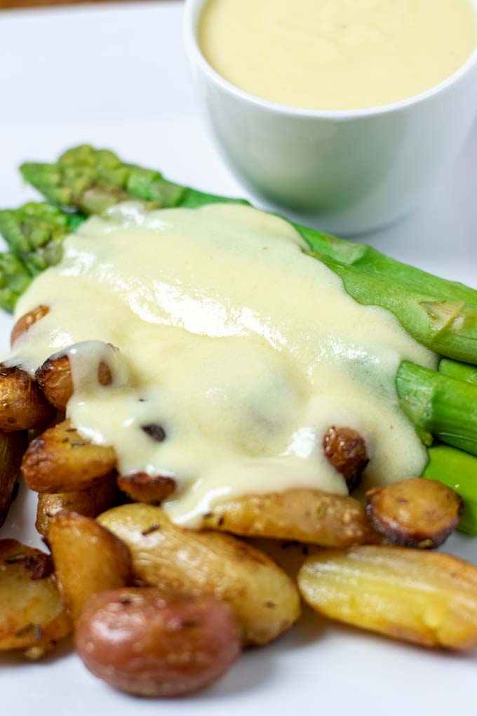 A portion of baked potatoes and green asparagus are served with the Mornay Sauce. A sauce boat is in the background. 