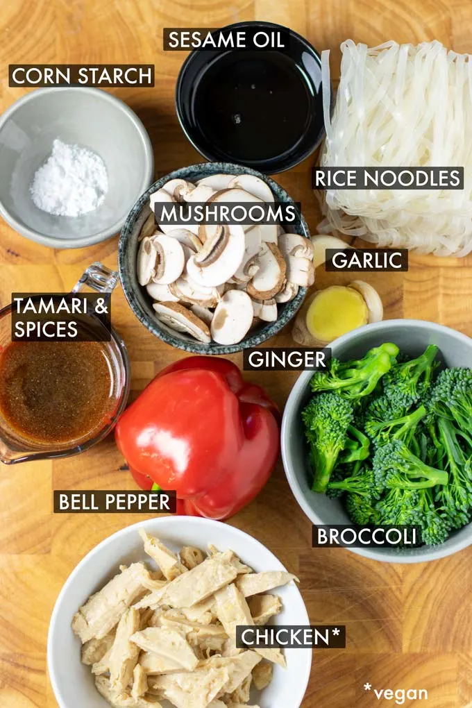 Ingredients needed to cook Rice Noodles are collected in small bowl on a wooden board. Text labels name the ingredients.