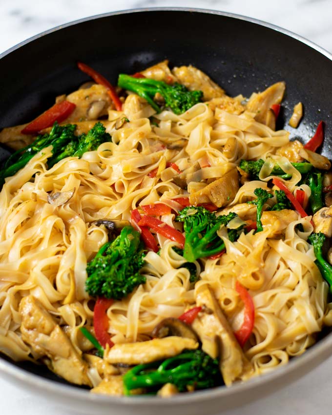 A large wok with rice noodles and the vegetable ingredients clearly visible.
