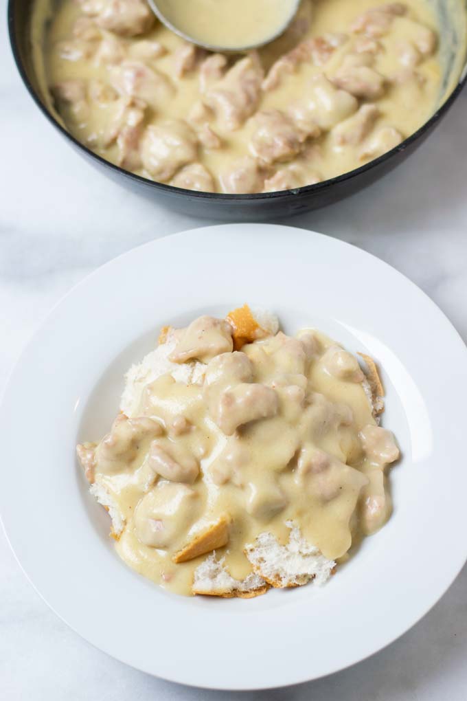 Portion of biscuits with Sausage Gravy on a plate with the pan in the background.