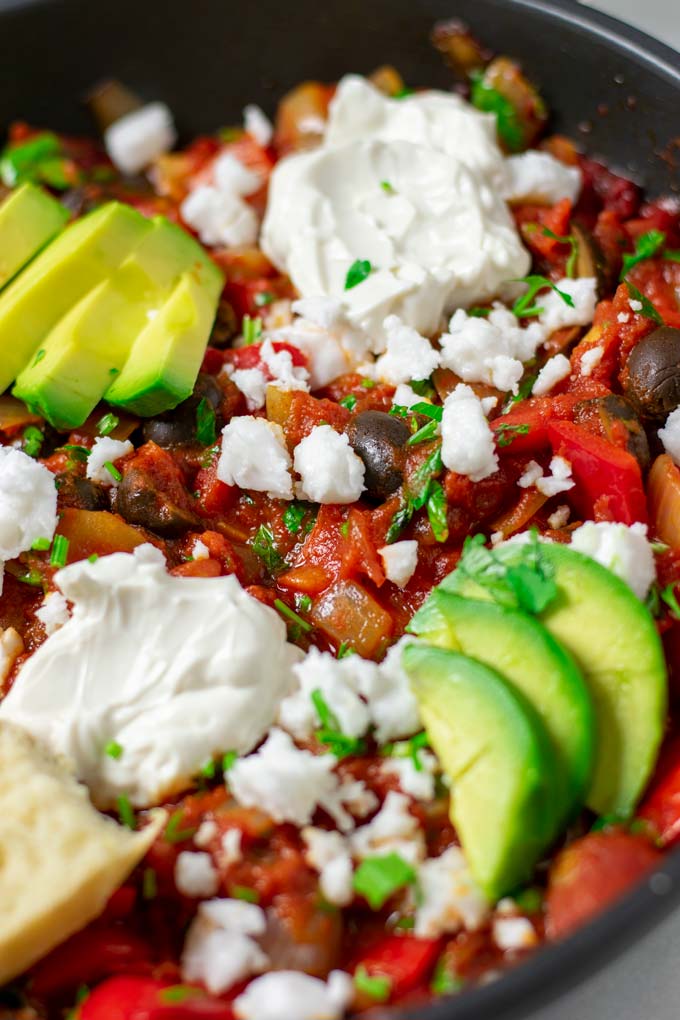 Closeup on the garnished Shakshuka showing the avocado slices and other toppings.