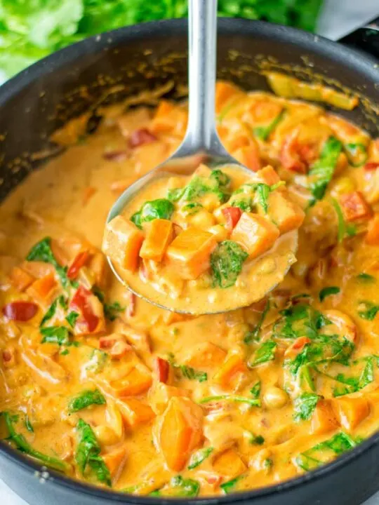 View of a big ladle with Sweet Potato Curry being lifted out of a large cooking pan.