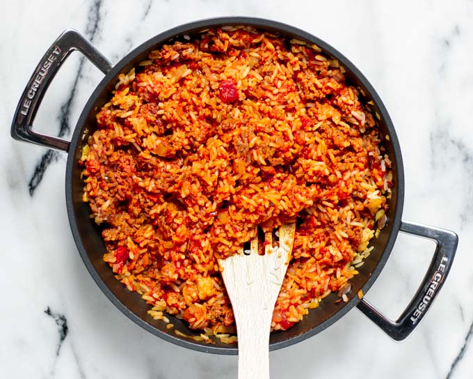 Top view of a pan with the Tomato Rice and a wooden spoon.