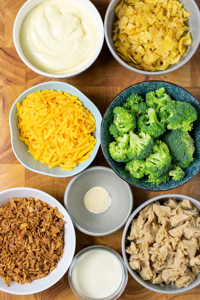 Ingredients for making the Chicken Broccoli Casserole are assembled in small bowls on a wooded board.