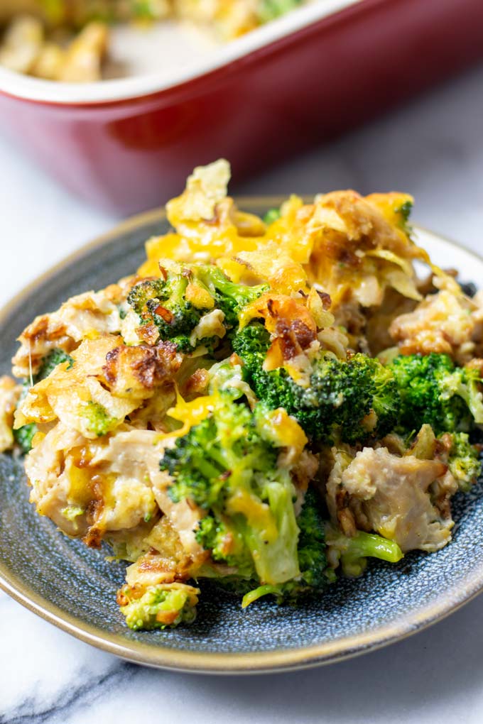 Closeup view on a portion of the Chicken Broccoli Casserole on a small blue plate with the casserole dish in the background.