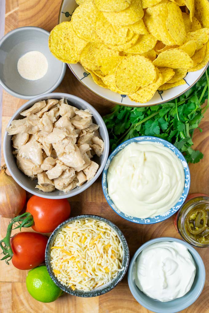 Ingredients needed to make Chicken Nachos are collected in small bowls on a wooden board.
