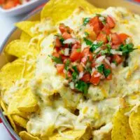 The Chicken Nachos from the oven are garnished with the fresh tomato topping. A small bowl with more of the topping is in the background.