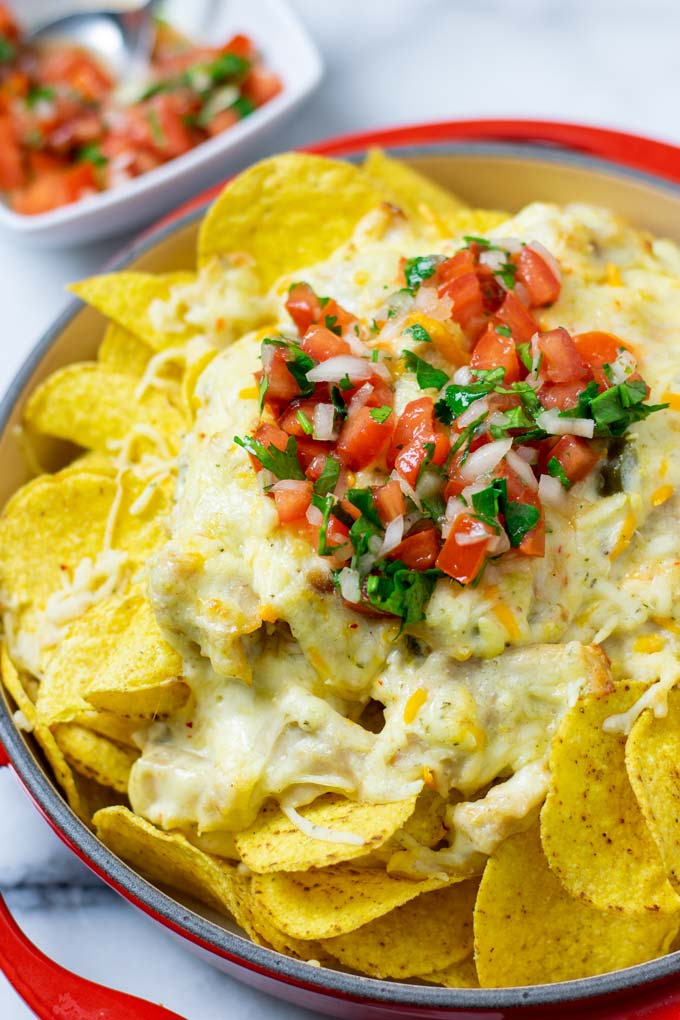 The Chicken Nachos from the oven are garnished with the fresh tomato topping. A small bowl with more of the topping is in the background.