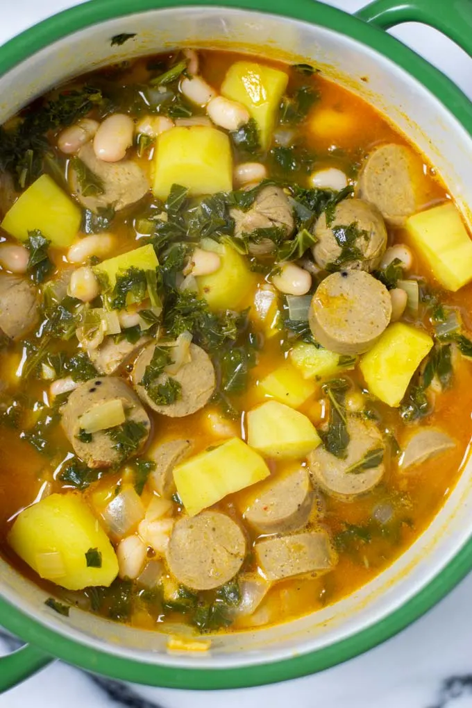 Top view on a large pot of the Kale Soup, showing the vegan sausage, potatoes, onions and kale ingredients. 