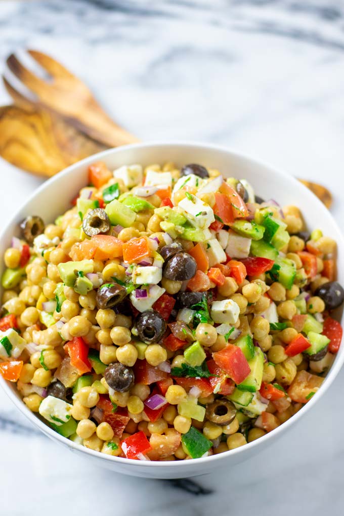 Side view of the Chickpea Salad in a serving bowl with wooden salad cutlery in the background.