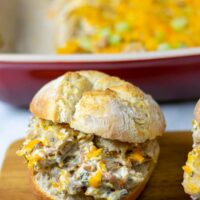 A Crack Chicken sandwich on a wooden serving board with the casserole dish in the background.