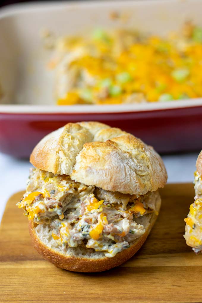 A Crack Chicken sandwich on a wooden serving board with the casserole dish in the background.