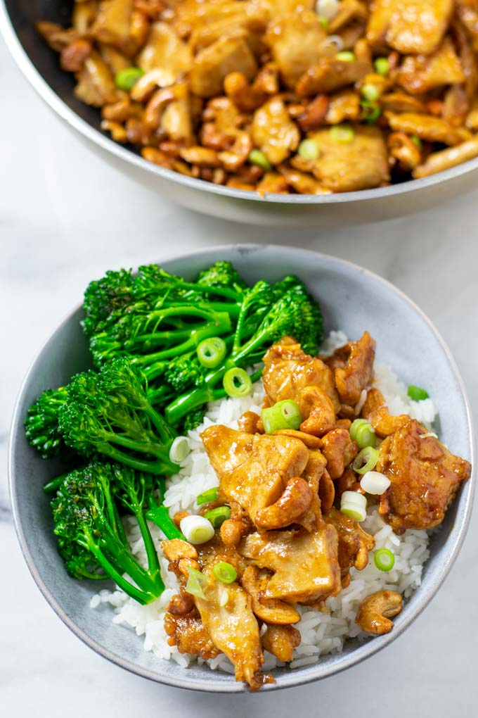 A serving portion of the Cashew Chicken with broccoli and rice in a bowl, with the pan in the background.