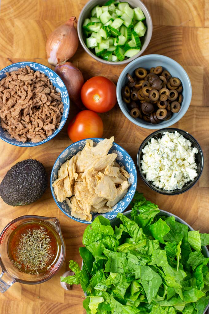 Ingredients for the Cobb Salad are assembled in small bowls on a wooden board.