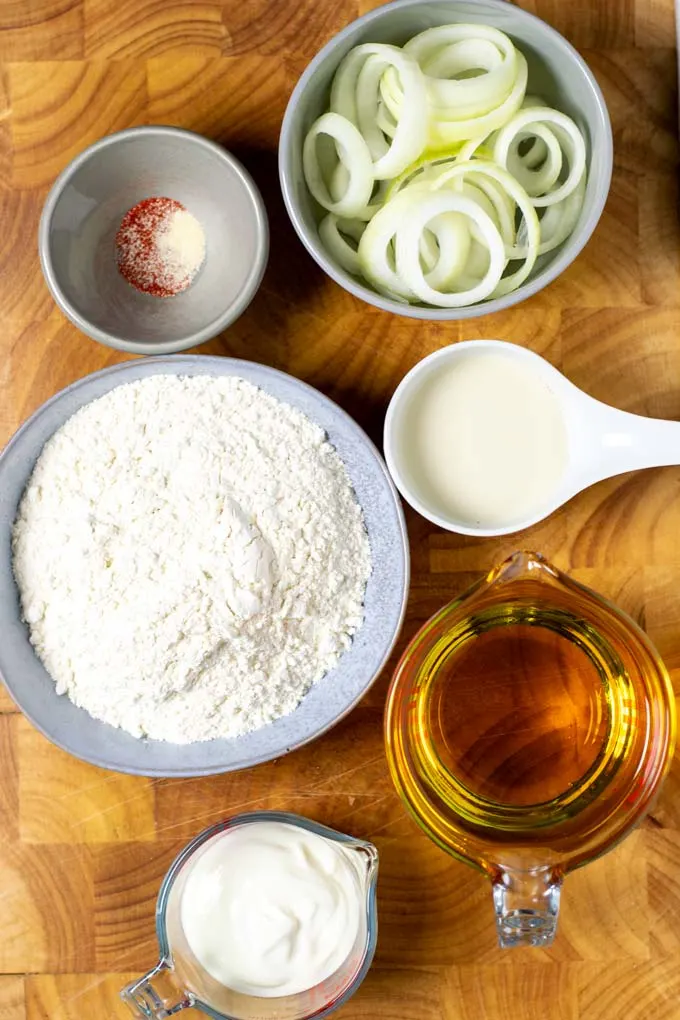 Ingredients needed for making Onion Rings are collected on a wooden board.