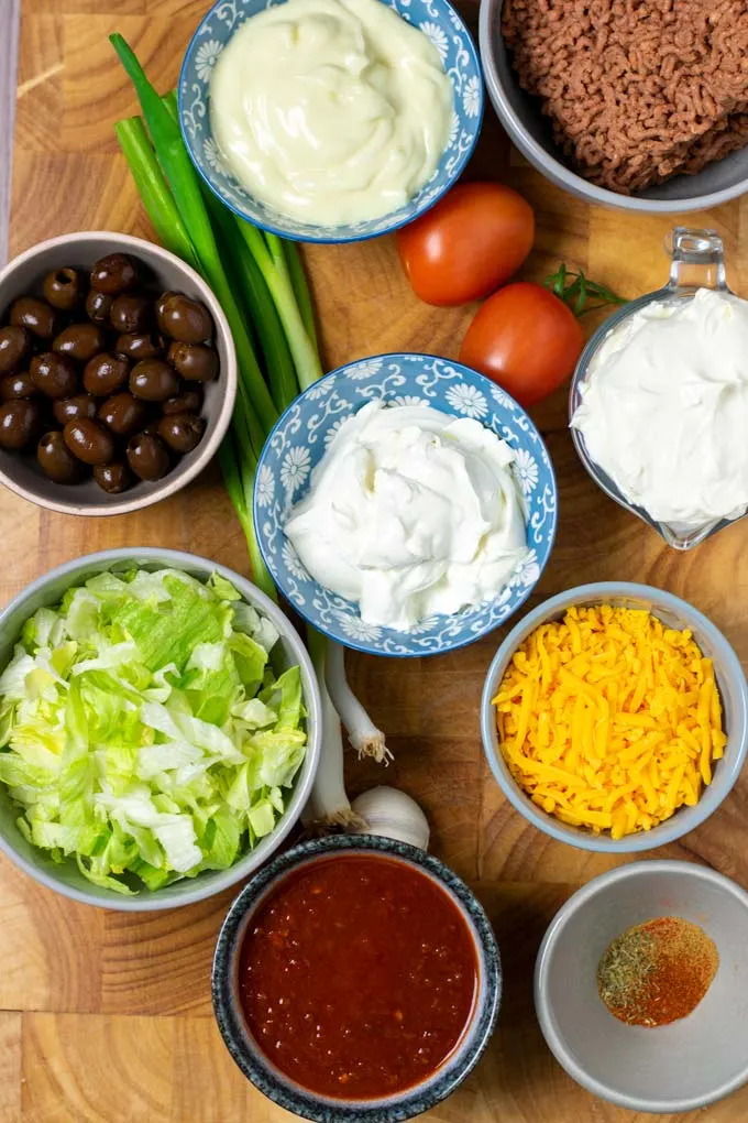 Assembly of all ingredients needed to make the Taco Dip on a wooden board.