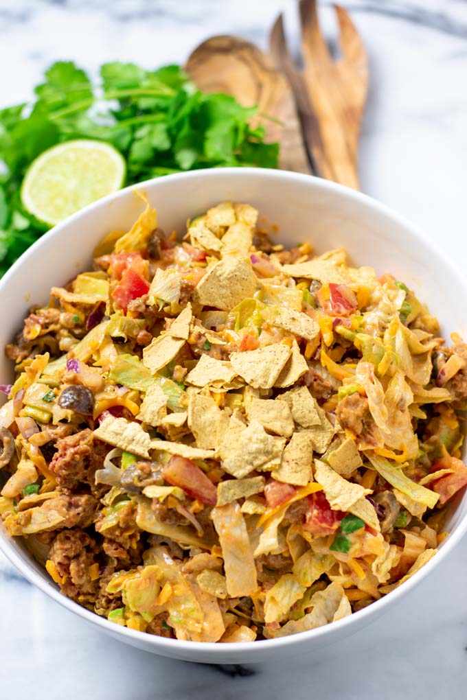 The finished Taco Salad in a large white bowl and fresh herbs in the background.