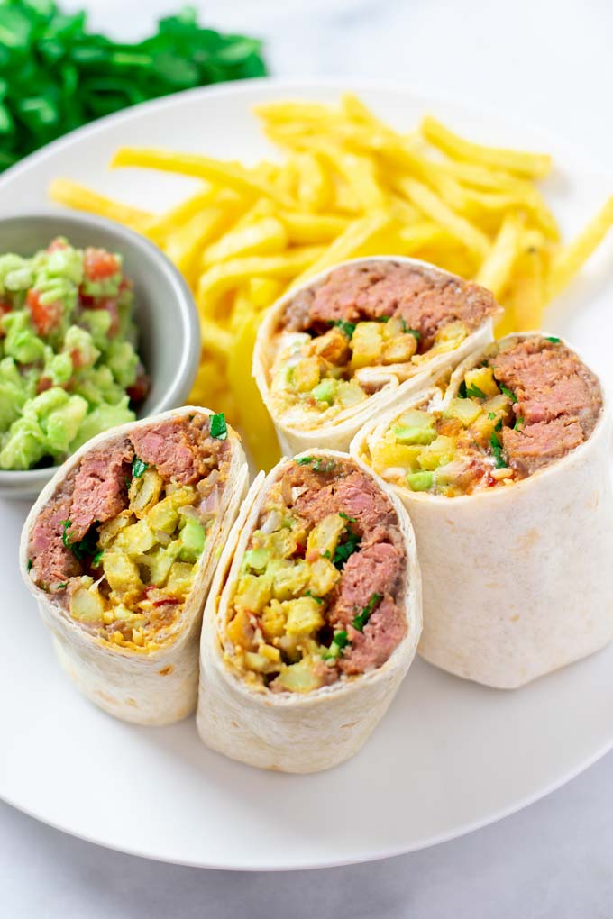 Two open cut California Burritos on a plate with extra fries and guacamole.