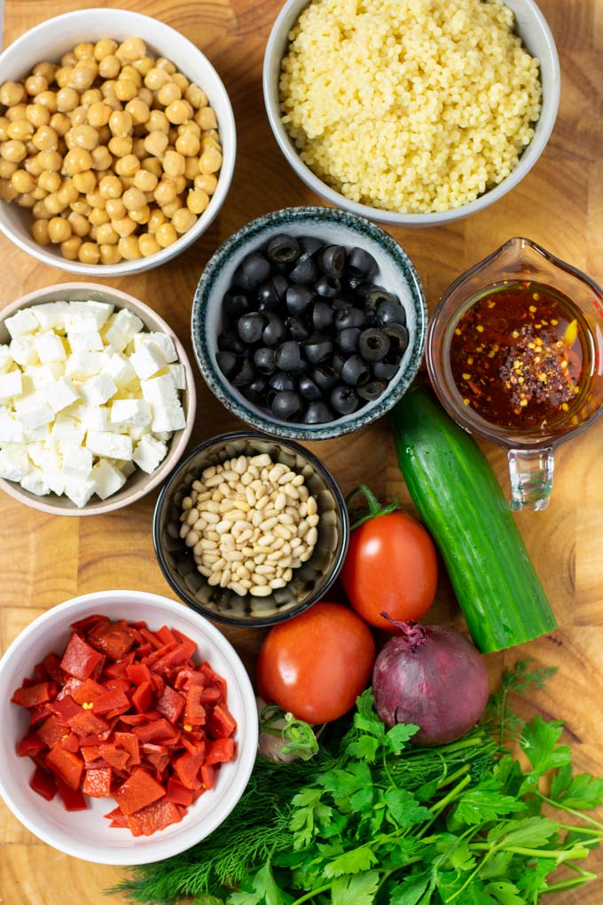 Ingredients needed to make the Couscous Salad are assembled in small bowls on a wooden board.