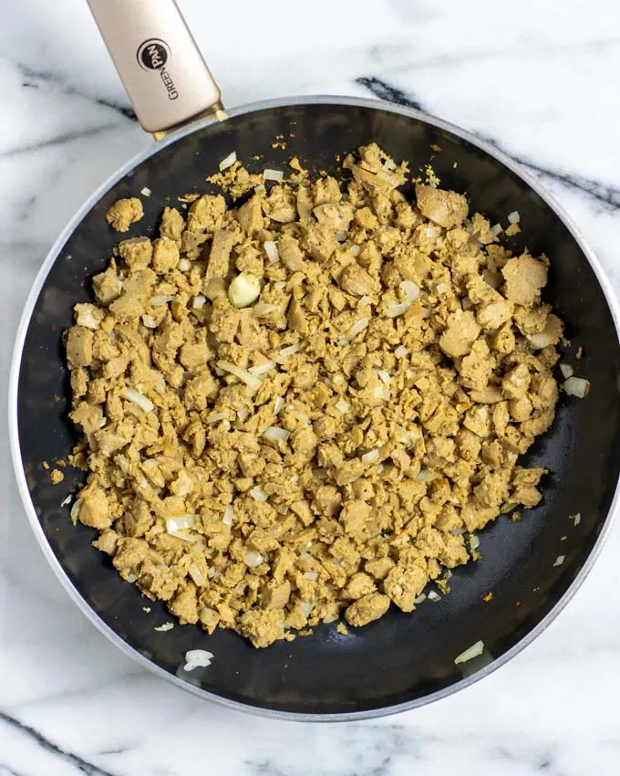 Showing how crumbled sausages are fried with onions in a pan.