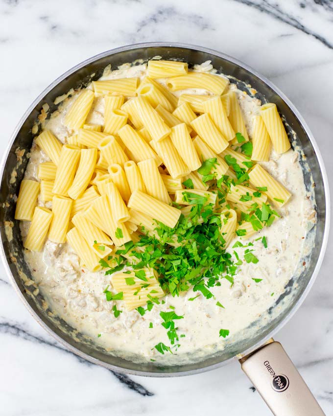 Showing how pre-cooked pasta and fresh herbs are given into the pan with the sauce.