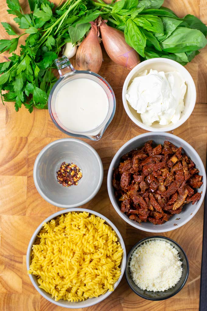 Ingredients for making the Sun Dried Tomato Pasta are collected on a wooden board.