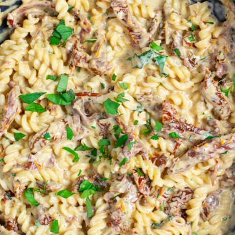 Top view on a pan full with the Sun Dried Tomato Pasta, garnished with extra fresh herbs.