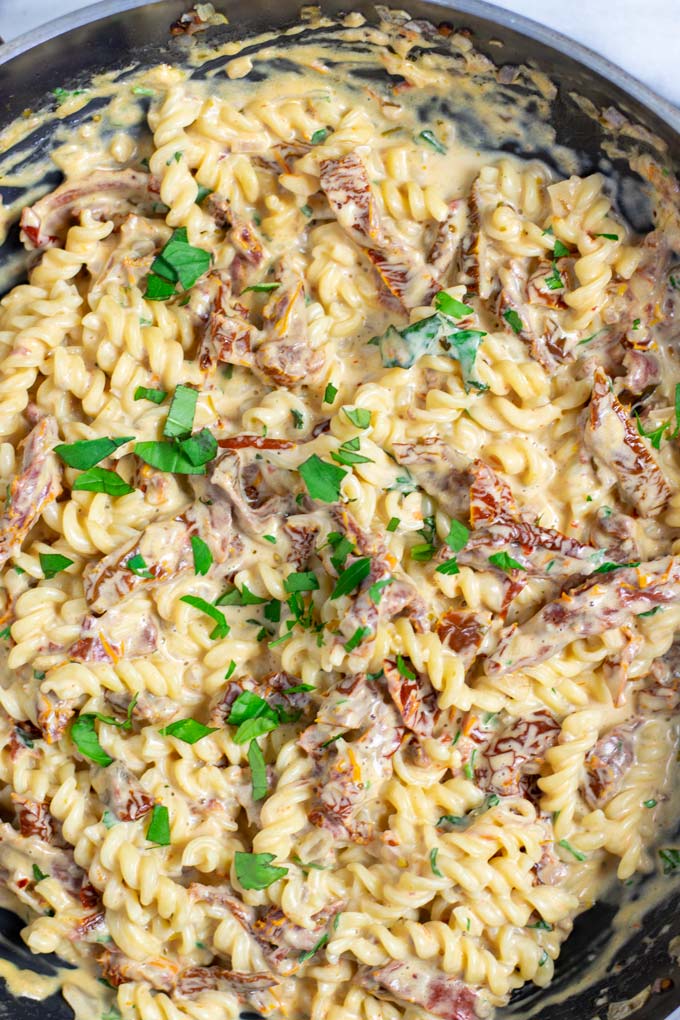 Top view on a pan full with the Sun Dried Tomato Pasta, garnished with extra fresh herbs.