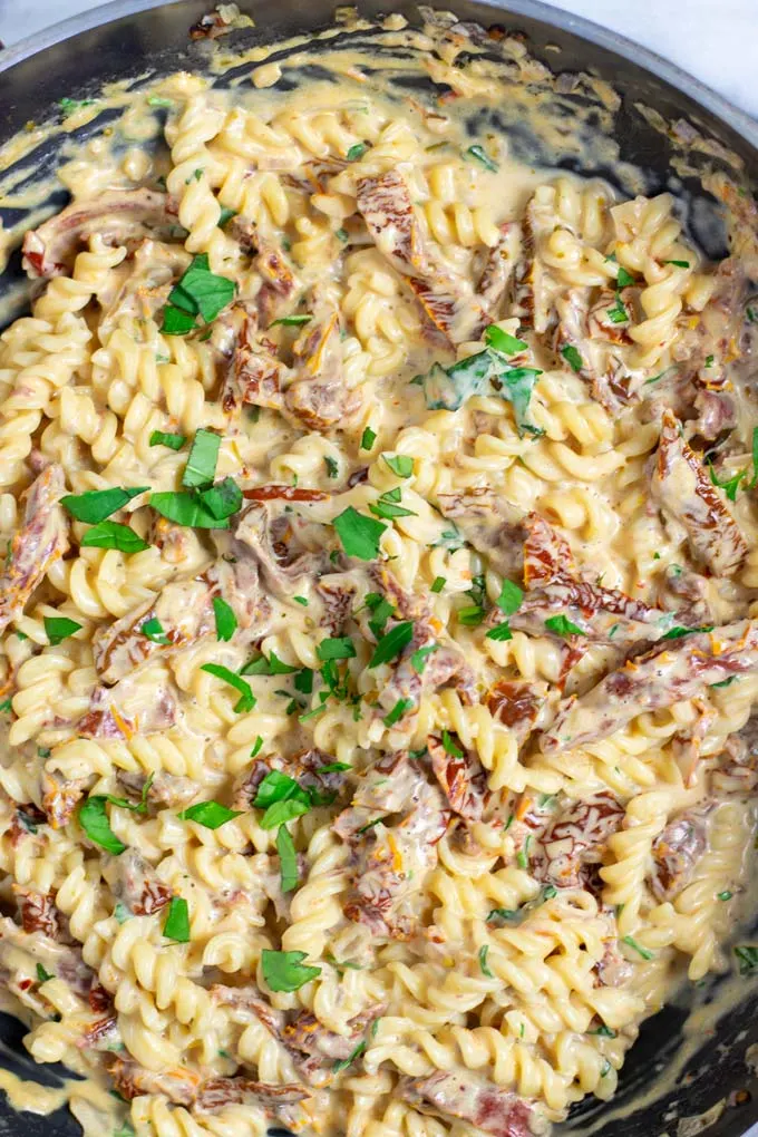 Top view on a pan full with the Sun Dried Tomato Pasta, garnished with extra fresh herbs.