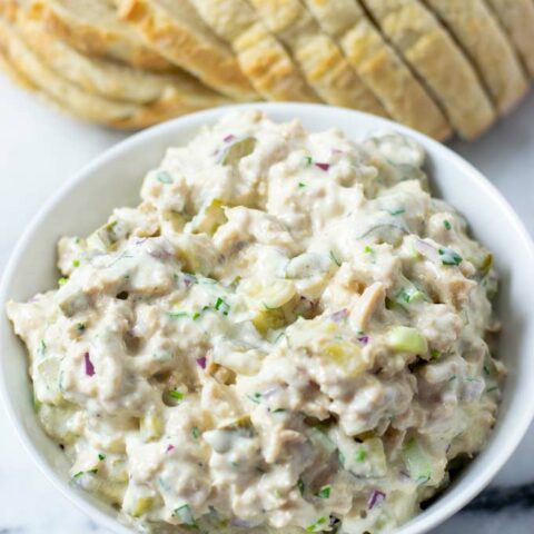 Closeup of a white serving bowl with the Tuna Salad and a loaf od fresh bread in the background.