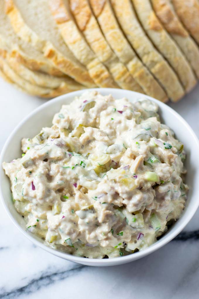 Closeup of a white serving bowl with the Tuna Salad and a loaf of fresh bread in the background.