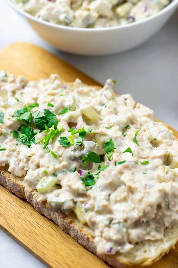 Closeup of a slice of bread with the Tuna Salad and garnished with fresh herbs.