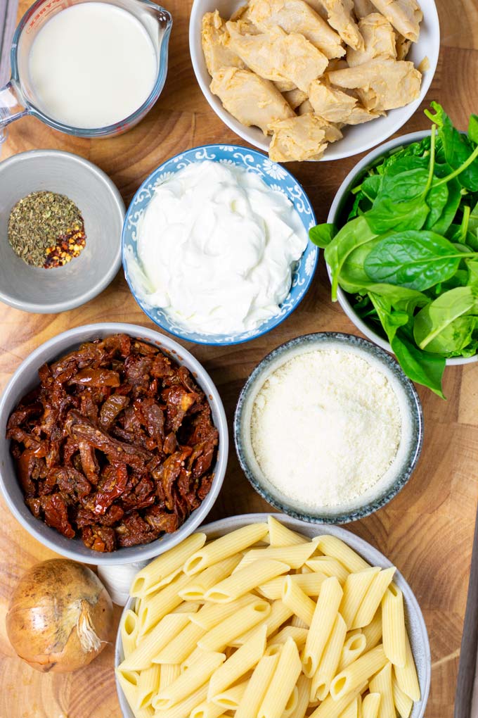 Ingredients for the Tuscan Chicken Pasta are assembled on a wooden board.