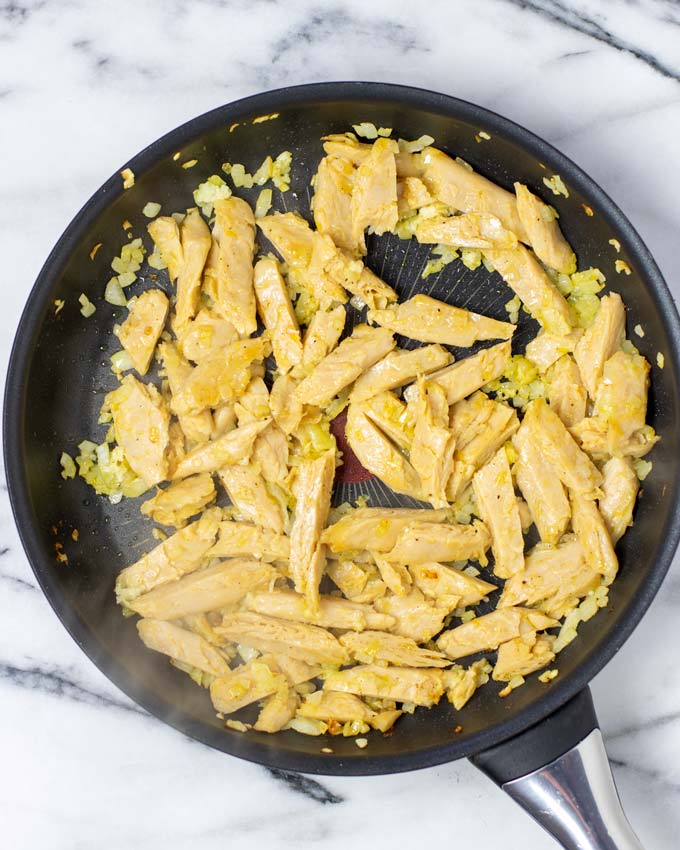 Showing a frying pan with fried vegan chicken stripes and onions.