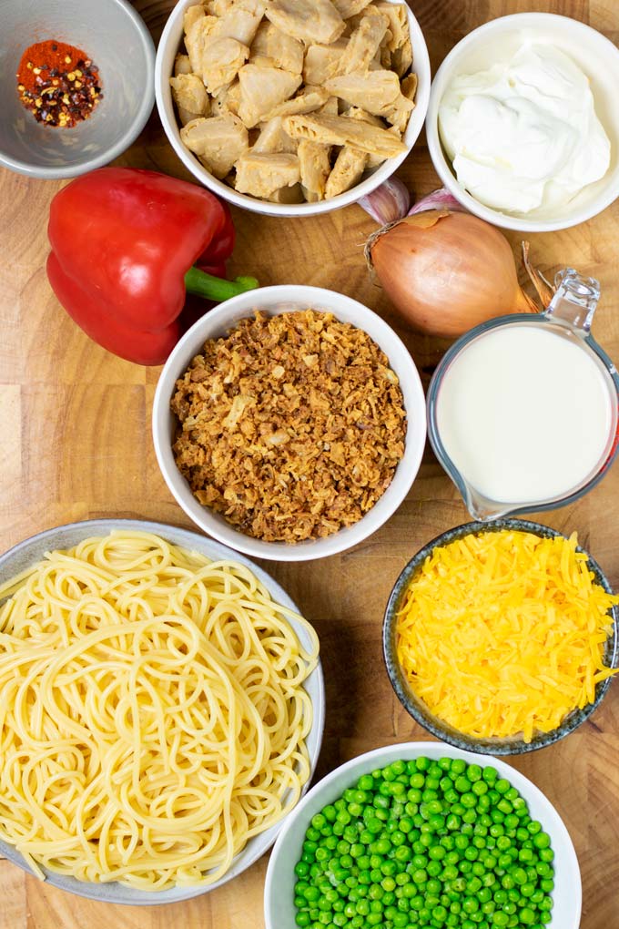 Ingredients needed to make Chicken Spaghetti are assembled in small bowls on a wooden board.